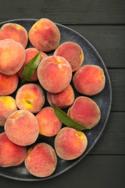 Tatlı şeftali ve yapraklar siyah tabakta, ahşap arka planda. Üst görünüm