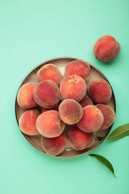 Tatlı şeftali ve yapraklar siyah tabakta ve naneli arkaplanda. Üst görünüm