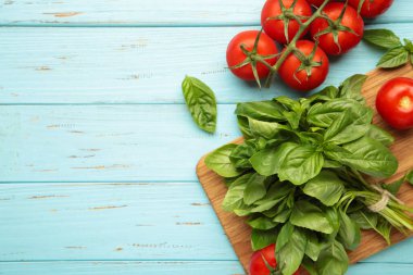 Mavi ahşap arka planda fesleğen yapraklı taze kiraz domatesleri. Üst görünüm