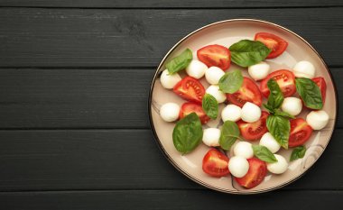 Çeri domatesli İtalyan Caprese salatası, mozzarella, siyah ahşap kaplamalı fesleğen. Üst görünüm