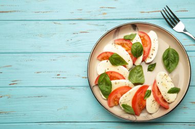 Çeri domatesli İtalyan Caprese salatası, mozzarella, çatallı fesleğen ve mavi ahşap arka plan. Metin için boşluk