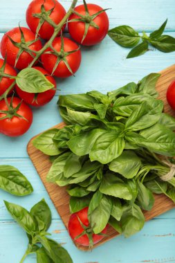 Mavi ahşap arka planda fesleğen yapraklı taze kiraz domatesleri. Üst görünüm