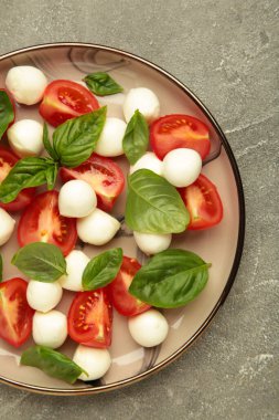 Çeri domatesli İtalyan Caprese salatası mozzarella, gri arka planda fesleğen. Üst görünüm