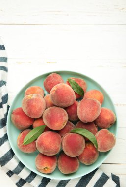 Tatlı şeftali ve yapraklar siyah tabakta beyaz arka planda. Üst görünüm