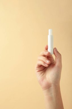 Bej arka planda doğal dudak kremi olan bir kadın eli. Üst görünüm