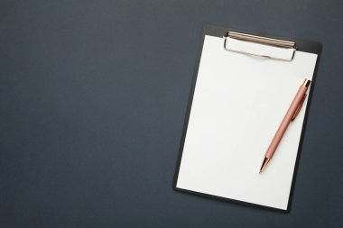 Koyu mavi arka planda boş kağıt ve kalemle siyah tablet. Üst görünüm