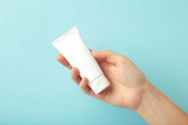 Mavi zemin üzerinde boş beyaz plastik bir tüp tutuyor. Kozmetik güzellik ürünü markalaşma modeli.