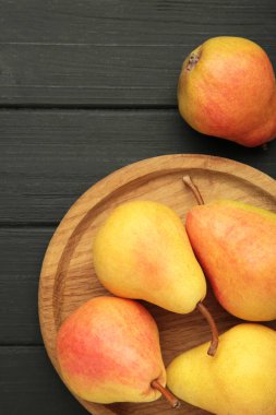 Taze armut meyvesi, ahşap tabakta, siyah arka planda. Dikey fotoğraf. Üst görünüm