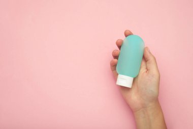 Pembe arka planda boş mavi plastik bir tüp tutuyor. Kozmetik güzellik ürünü markalaşma modeli.