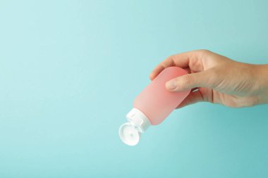 Mavi arka planda boş pembe plastik bir tüp tutuyor. Kozmetik güzellik ürünü markalaşma modeli.