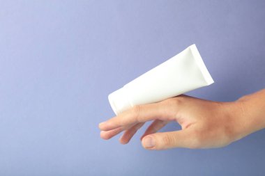 Mor zemin üzerinde boş beyaz plastik bir tüp tutuyor. Kozmetik güzellik ürünü markalaşma modeli.