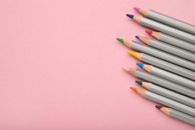 Pembe arka planda bir sürü renkli kalem var. Üst görünüm