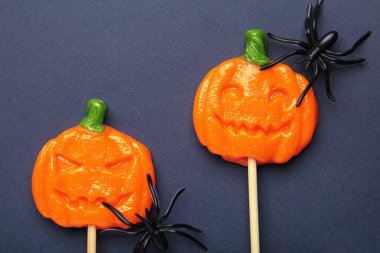 Cadılar Bayramı lolipopları, lacivert arka planda dekoratif örümcekli balkabağı şeklinde. Mevsimsel kutlamalar için bayram ziyafetleri. Üst görünüm