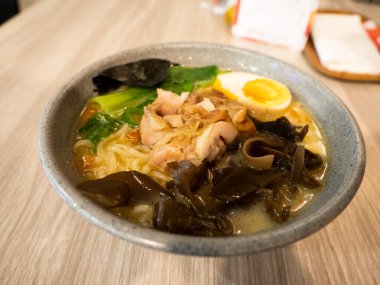 Tahta bir masanın üzerinde yumurta, mantar, erişte ve sebze içeren bir kase ramen.