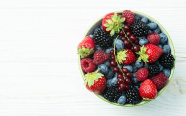 Kase fotoğrafında olgun renkli böğürtlenlerin karışımı. Yabanmersini, çilek, ahududu, böğürtlen ve frenk üzümü. Kırsal arkaplanda üst görünüm