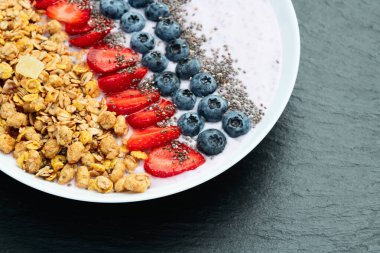 Sağlıklı kahvaltı. Çilekli yoğurt (çilek, ahududu, yabanmersini, böğürtlen), granola ve chia tohumları. Kırsal arkaplanda üst görünüm