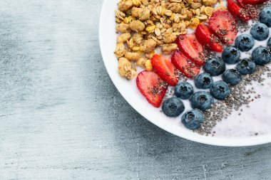 Sağlıklı kahvaltı. Çilekli yoğurt (çilek, ahududu, yabanmersini, böğürtlen), granola ve chia tohumları. Kırsal arkaplanda üst görünüm