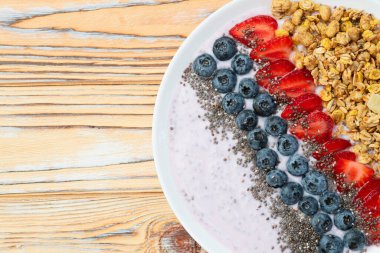 Sağlıklı kahvaltı. Çilekli yoğurt (çilek, ahududu, yabanmersini, böğürtlen), granola ve chia tohumları. Kırsal arkaplanda üst görünüm