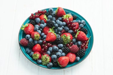 Kase fotoğrafında olgun renkli böğürtlenlerin karışımı. Yabanmersini, çilek, ahududu, böğürtlen ve frenk üzümü. Kırsal arkaplanda üst görünüm