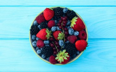 Kase fotoğrafında olgun renkli böğürtlenlerin karışımı. Yabanmersini, çilek, ahududu, böğürtlen ve frenk üzümü. Kırsal arkaplanda üst görünüm