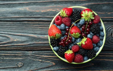Kase fotoğrafında olgun renkli böğürtlenlerin karışımı. Yabanmersini, çilek, ahududu, böğürtlen ve frenk üzümü. Kırsal arkaplanda üst görünüm