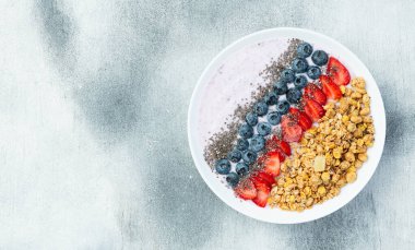 Sağlıklı kahvaltı. Çilekli yoğurt (çilek, ahududu, yabanmersini, böğürtlen), granola ve chia tohumları. Kırsal arkaplanda üst görünüm