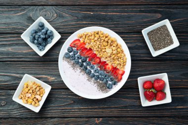 Sağlıklı kahvaltı. Çilekli yoğurt (çilek, ahududu, yabanmersini, böğürtlen), granola ve chia tohumları. Kırsal arkaplanda üst görünüm