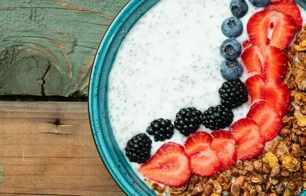 Sağlıklı kahvaltı. Çilekli yoğurt (çilek, ahududu, yabanmersini, böğürtlen), granola ve chia tohumları. Kırsal arkaplanda üst görünüm