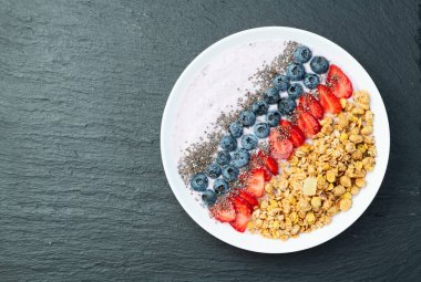 Sağlıklı kahvaltı. Çilekli yoğurt (çilek, ahududu, yabanmersini, böğürtlen), granola ve chia tohumları. Kırsal arkaplanda üst görünüm