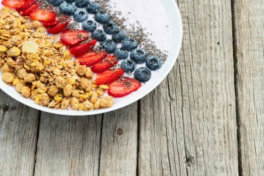 Sağlıklı kahvaltı. Çilekli yoğurt (çilek, ahududu, yabanmersini, böğürtlen), granola ve chia tohumları. Kırsal arkaplanda üst görünüm