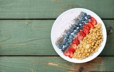 Sağlıklı kahvaltı. Çilekli yoğurt (çilek, ahududu, yabanmersini, böğürtlen), granola ve chia tohumları. Kırsal arkaplanda üst görünüm