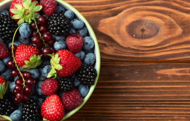 Kase fotoğrafında olgun renkli böğürtlenlerin karışımı. Yabanmersini, çilek, ahududu, böğürtlen ve frenk üzümü. Kırsal arkaplanda üst görünüm