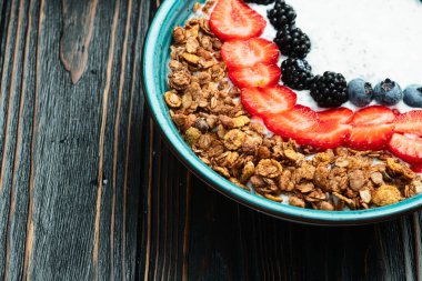 Sağlıklı kahvaltı. Çilekli yoğurt (çilek, ahududu, yabanmersini, böğürtlen), granola ve chia tohumları. Kırsal arkaplanda üst görünüm