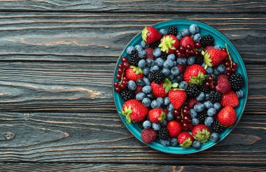 Kase fotoğrafında olgun renkli böğürtlenlerin karışımı. Yabanmersini, çilek, ahududu, böğürtlen ve frenk üzümü. Kırsal arkaplanda üst görünüm