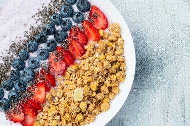 Sağlıklı kahvaltı. Çilekli yoğurt (çilek, ahududu, yabanmersini, böğürtlen), granola ve chia tohumları. Kırsal arkaplanda üst görünüm