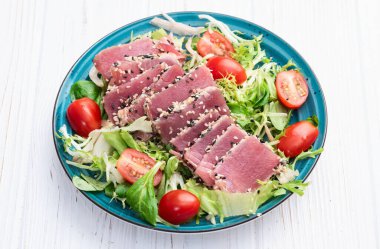Çiğ ton balığı, susam ve vişneli domates fotoğraflı salata. Kırsal arkaplanda üst görünüm