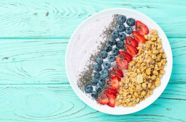 Sağlıklı kahvaltı. Çilekli yoğurt (çilek, ahududu, yabanmersini, böğürtlen), granola ve chia tohumları. Kırsal arkaplanda üst görünüm