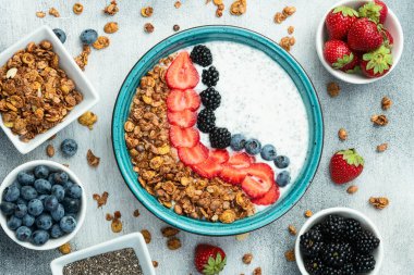 Sağlıklı kahvaltı. Çilekli yoğurt (çilek, ahududu, yabanmersini, böğürtlen), granola ve chia tohumları. Kırsal arkaplanda üst görünüm
