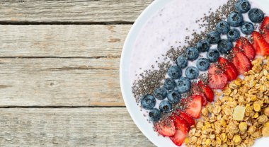 Sağlıklı kahvaltı. Çilekli yoğurt (çilek, ahududu, yabanmersini, böğürtlen), granola ve chia tohumları. Kırsal arkaplanda üst görünüm