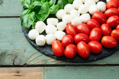 Fesleğen yaprakları, kiraz domatesleri ve mozzarella peyniri. İtalyan bayrağı gibi yiyecek fotoğrafçılığı. Üst görünüm