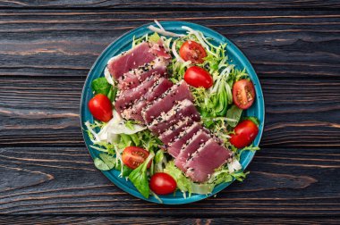 Çiğ ton balığı, susam ve vişneli domates fotoğraflı salata. Kırsal arkaplanda üst görünüm