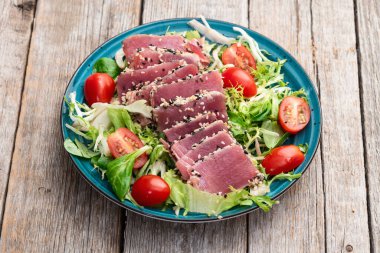 Çiğ ton balığı, susam ve vişneli domates fotoğraflı salata. Kırsal arkaplanda üst görünüm