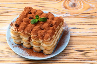 Kakao tozuyla kaplı lezzetli bir tiramisu ve taze nane yapraklarıyla süslenmiş, kırsal ahşap bir masada servis ediliyor.