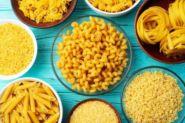 Penne, fusilli ve tagliatelle gibi çeşitli pişmemiş makarna çeşitleri kırsal ahşap bir yüzeyde kaselerde sergilenir. üst yaşam