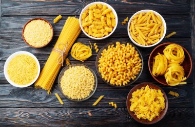 Penne, fusilli ve tagliatelle gibi çeşitli pişmemiş makarna çeşitleri kırsal ahşap bir yüzeyde kaselerde sergilenir. üst yaşam