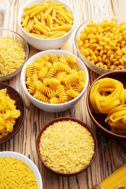 Penne, fusilli ve tagliatelle gibi çeşitli pişmemiş makarna çeşitleri kırsal ahşap bir yüzeyde kaselerde sergilenir. üst yaşam