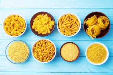 Penne, fusilli ve tagliatelle gibi çeşitli pişmemiş makarna çeşitleri kırsal ahşap bir yüzeyde kaselerde sergilenir. üst yaşam