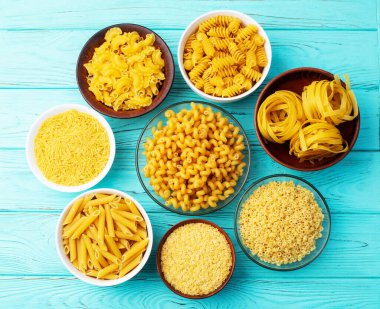 Penne, fusilli ve tagliatelle gibi çeşitli pişmemiş makarna çeşitleri kırsal ahşap bir yüzeyde kaselerde sergilenir. üst yaşam