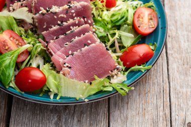 Çiğ ton balığı, susam ve vişneli domates fotoğraflı salata. Kırsal arkaplanda üst görünüm