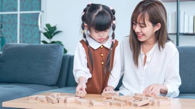 Yaratıcı oyun, hayal gücü çocuk ve oyuncak. Sevimli anne ve çocuğu tahta tuğla oyuncaklarıyla oynuyorlar. Mutlu aile Asya anne ve kızı modern oturma odasında oyuncak bloklarıyla oynuyorlar..